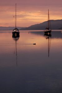 Silhouette of sailboats in sea against sunset sky