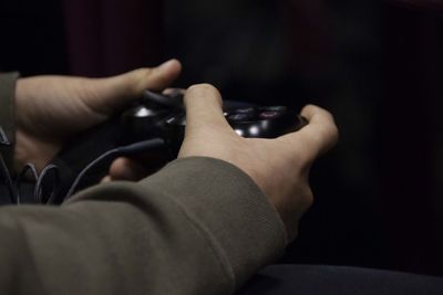 Cropped hands of person playing video game against black background