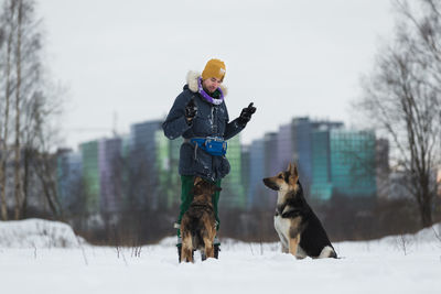 Man standing by dogs on snow covered land against sky