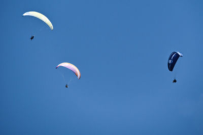 Low angle view of people paragliding against sky