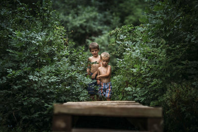 Full length of shirtless boy standing against trees