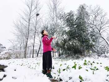 Woman standing on snow covered field against trees