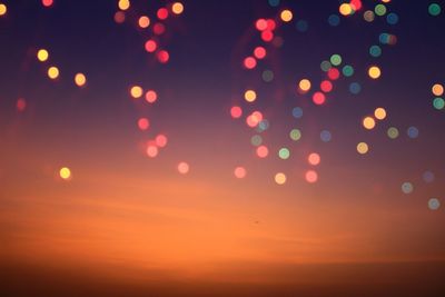 Defocused image of illuminated lights against sky at night