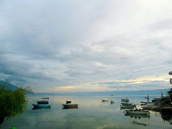 Boats in sea against cloudy sky