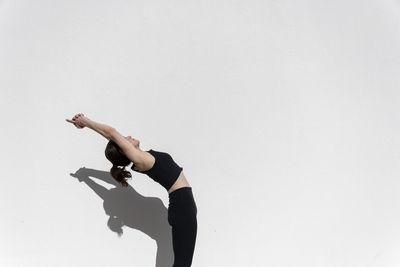 Woman doing a mountain pose with backbend, yoga outdoors, white wall background.