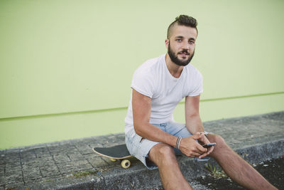 Portrait of man with smartphone sitting on his skateboard at carb