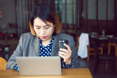 Young woman using phone while sitting on table