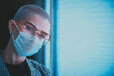 Portrait of young woman with shaved head wearing mask standing against abstract backgrounds