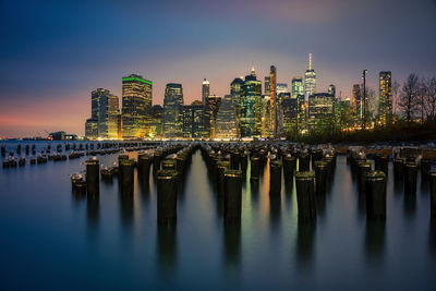 Illuminated modern building by river against sky at dusk