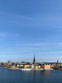 View of buildings by river against blue sky