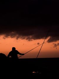 Silhouette man fishing against orange sky at beach