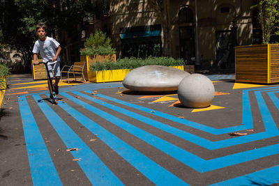 A child rides a scooter in a public space with street furniture located in barcelona, spain.