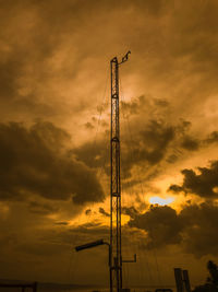 Low angle view of silhouette crane against dramatic sky during sunset