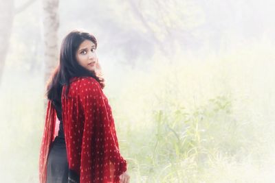 Portrait of beautiful young woman standing against red background