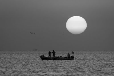 Silhouette people on boat sailing in sea against clear sky