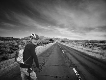 Man sitting on bicycle on road against sky