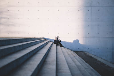 Side view of woman sitting on steps against gray wall