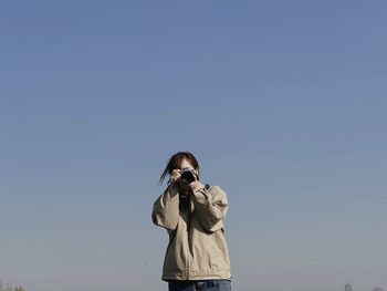 Side view of woman photographing against sky