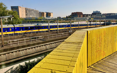 Train passing footbridge in city against sky