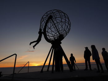 Silhouette people on water against clear sky during sunset