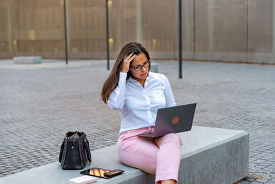 Young woman using mobile phone while sitting on laptop