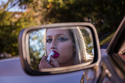 Reflection of woman applying lipstick seen in side-view mirror