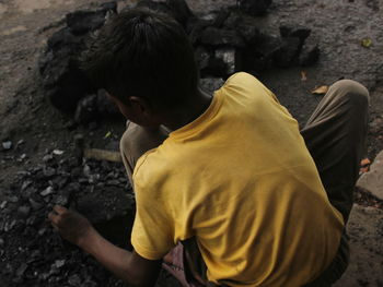 Rear view of boy breaking coals while crouching on rock