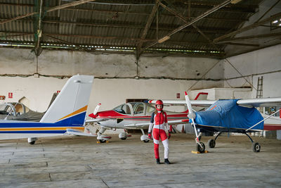 Young female skydiver in a plane hangar surrounded by planes