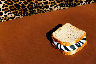 Crop anonymous person in shirt with leopard print sitting at brown table with sandwich with zebra filling in light room