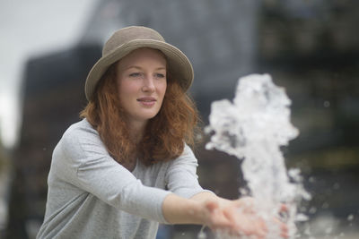 Young woman with hat outside playing with a water fountain