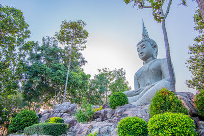 Low angle view of statue by trees against sky