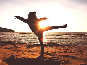 Silhouette woman balancing at beach against sky during sunset