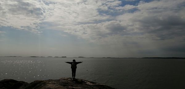 Rear view of man standing on rock by sea against sky