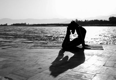Silhouette of woman doing yoga by lake