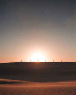 Scenic view of people on sand dune during sunset