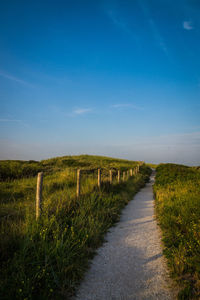 Road passing through field against blue sky