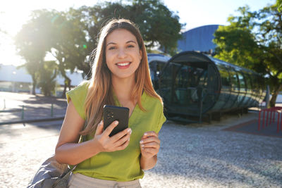 Portrait of happy smiling young woman looking at camera holding phone in curitiba, brazil