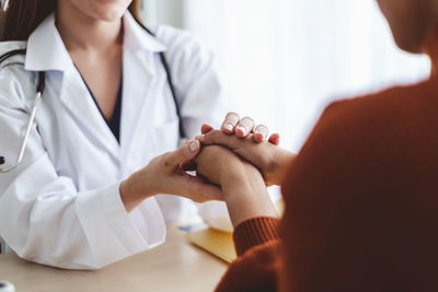 Midsection of female doctor holding hand of patient at hospital