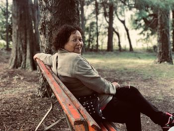 Portrait of woman sitting on bench in forest