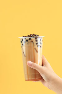 Cropped hand holding drink against yellow background