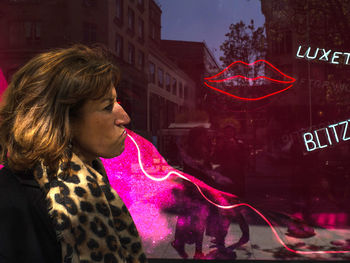Portrait of young woman looking at illuminated building