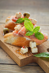 Bruschetta with smoked salmon, cream cheese, olives and arugula on rustic wooden plate