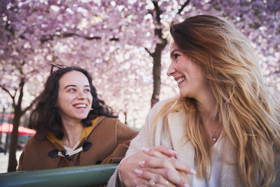 Smiling young women standing under cherry blossom