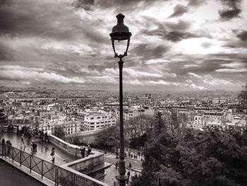 Street lamp by cityscape against sky