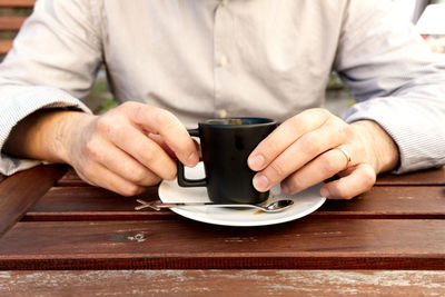 Midsection of man holding coffee cup on table