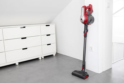 Modern cordless vacuum cleaner leaning on a wall of a room. homework concept