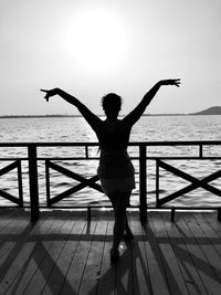 Woman with arms outstretched dancing by railing against sea