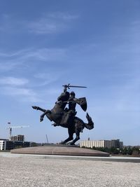 Statue by street against blue sky