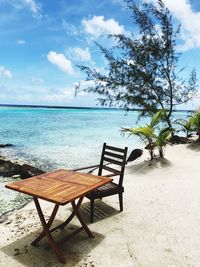 Empty chair and table at beach against sky