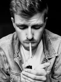 Young man smoking cigarette against black background